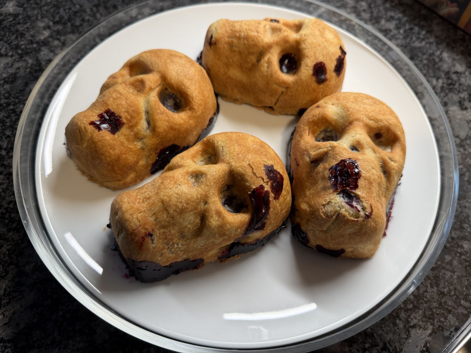 Spooky golden skull-shaped blueberry pies with bubbling purple filling.