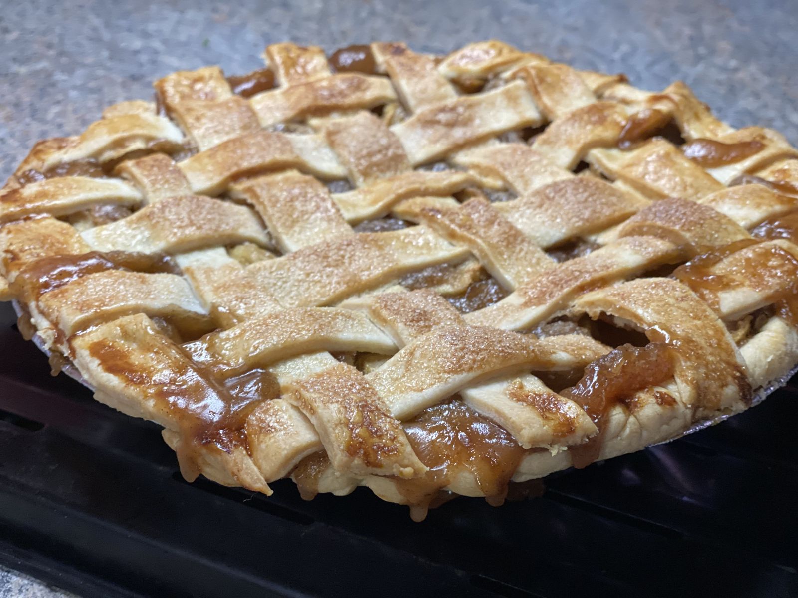 A golden-brown lattice-topped Granny Smith apple pie on a cooling rack.