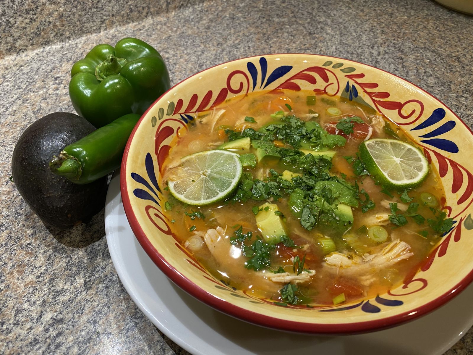 A bowl of Sopa de Lima topped with tortilla strips, avocado, and cilantro.